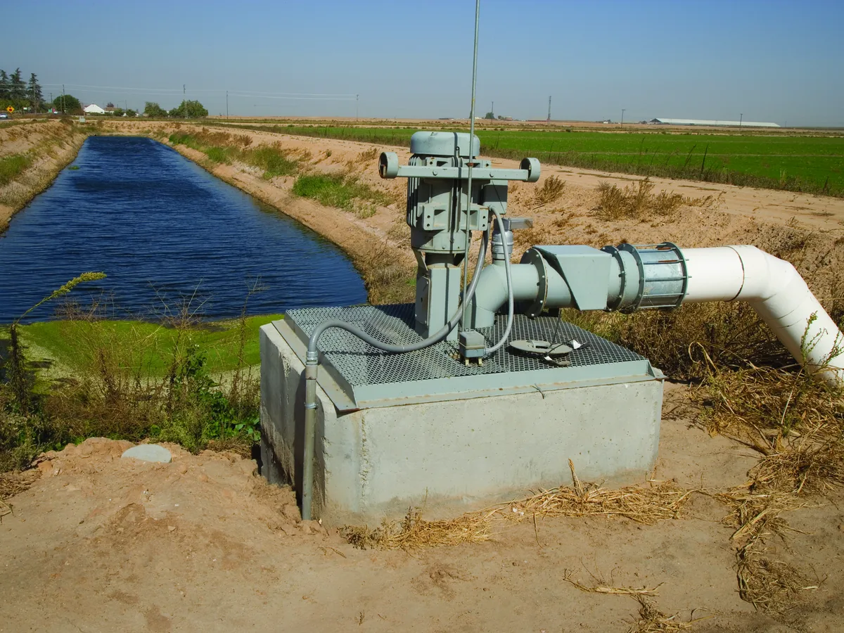 Vertical irrigation pump and motor on a concrete sump beside a canal