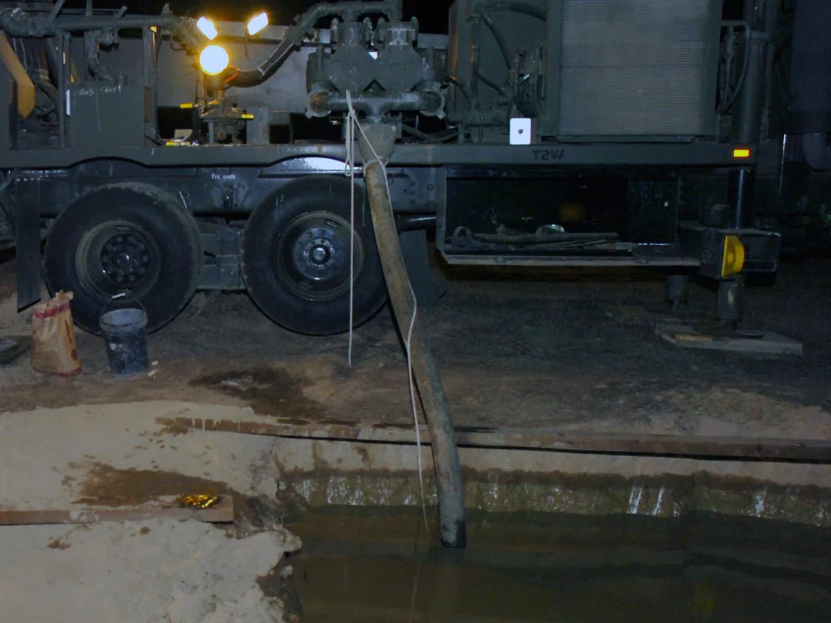 Drill rig working at night under work lights beside a mud pit