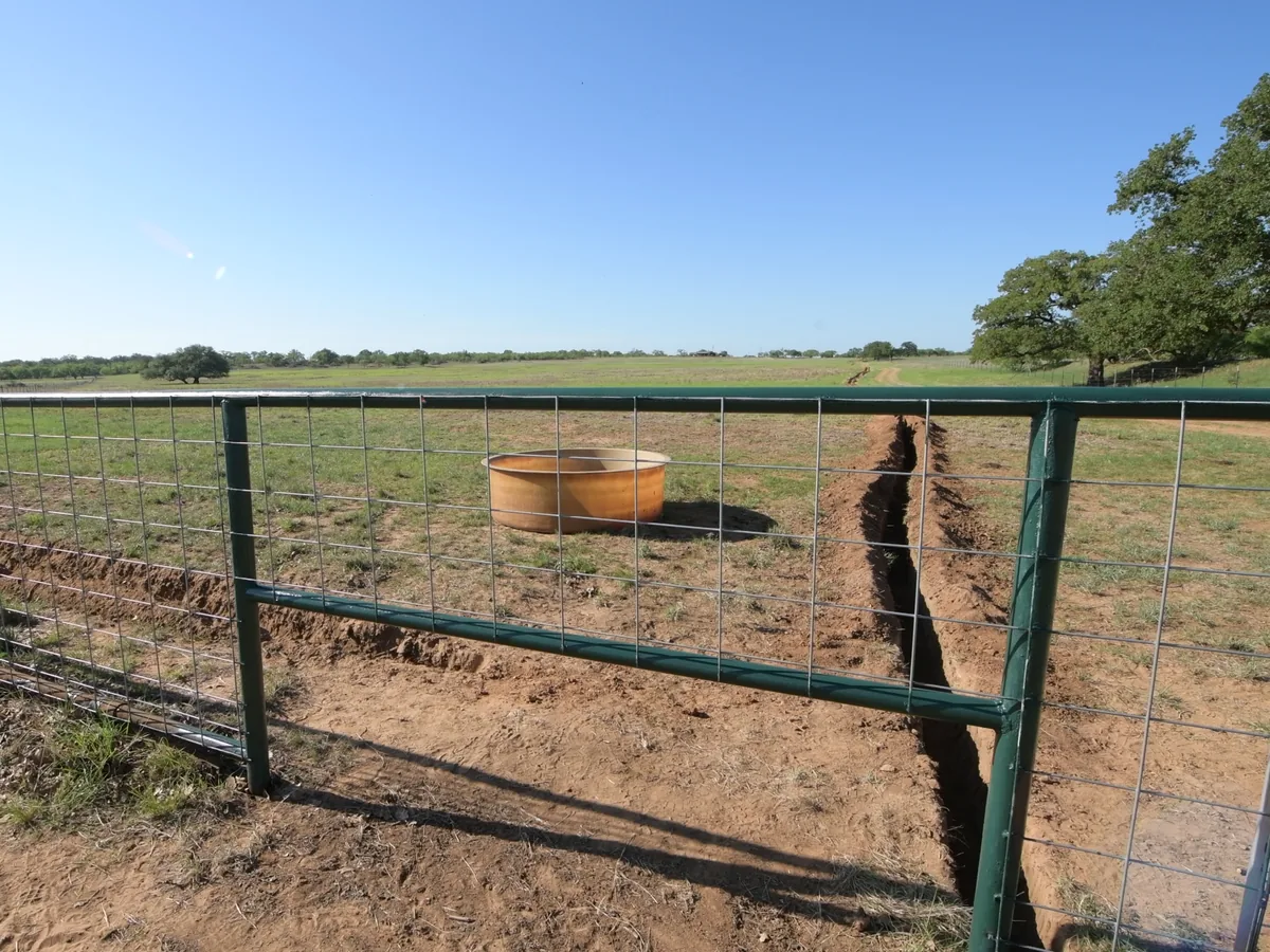 Open trench cut across a pasture toward a water trough