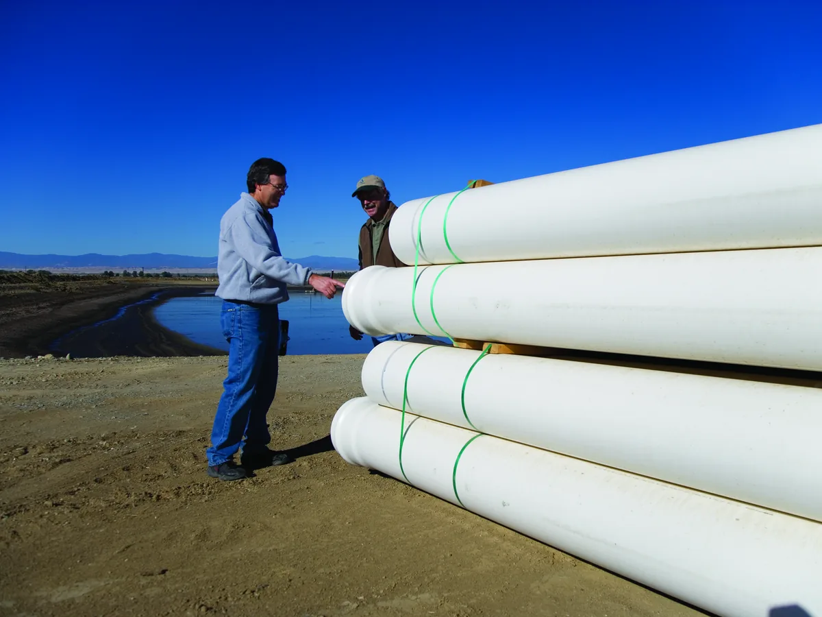 Two men inspecting stacks of white plastic pipe for an underground water line