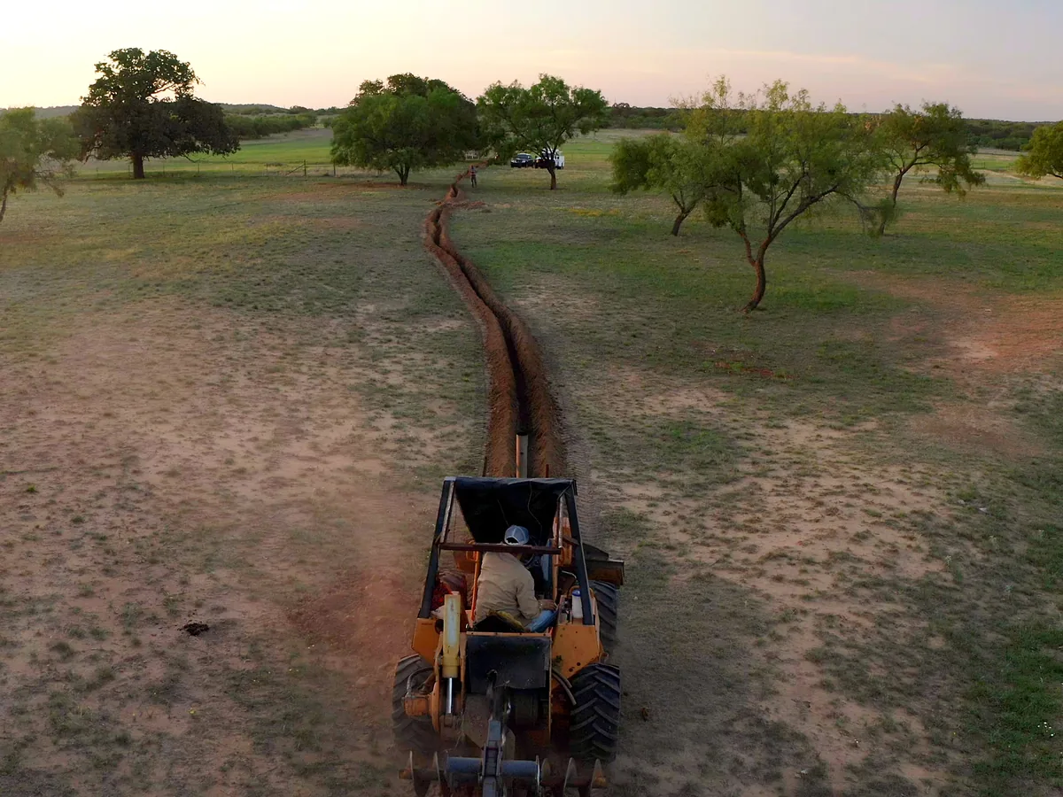 Aerial view of a trencher cutting a long trench across a pasture