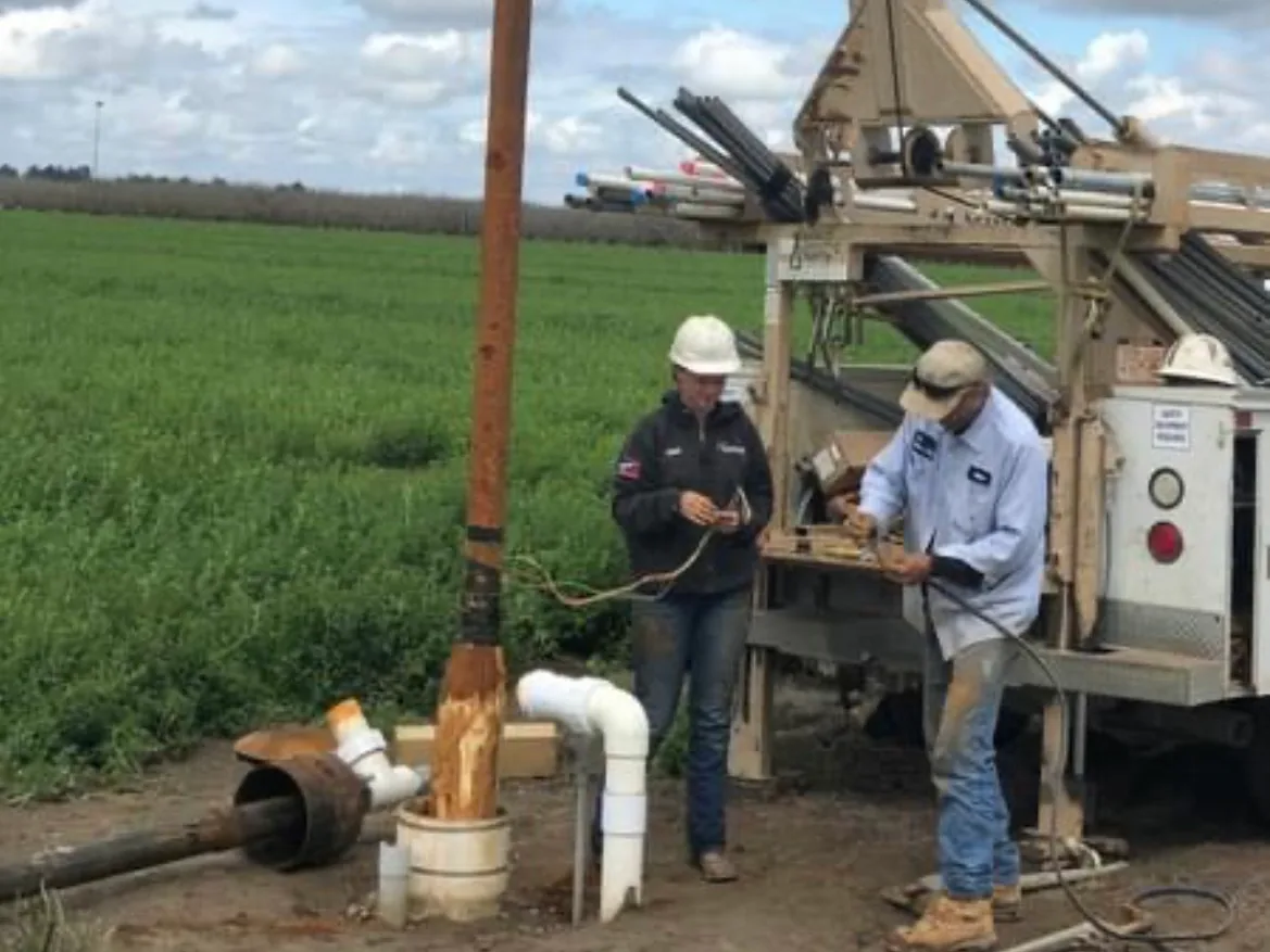 Two crew members working at the well head beside a drill rig in a green field