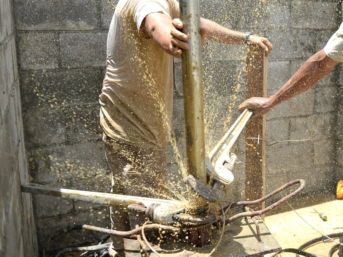 Two workers with pipe wrenches breaking a drop pipe joint at a well head during a pump replacement