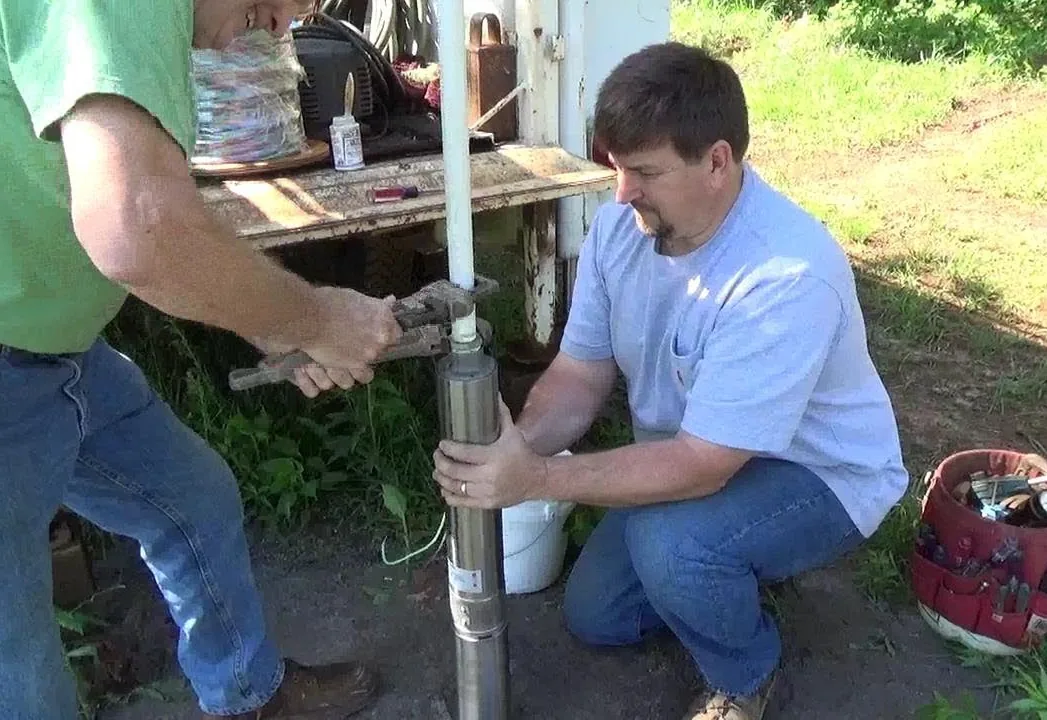 Two workers fitting drop pipe to a new submersible pump during a pump installation
